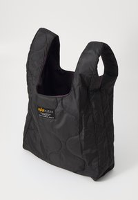 Sac fourré noir avec des motifs cousus courbes, deux poignées courtes et une doublure intérieure violette. Présente une petite étiquette de logo.