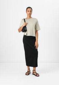 Loose, short-sleeved, light gray top paired with a form-fitting black maxi skirt and black strappy sandals. Holds a small black bag.