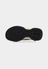 Πάτος ενός μπεζ και μαύρου αθλητικού παπουτσιού με κυκλικά σχέδια πέλματος και το όνομα της μάρκας Geox στη φτέρνα.