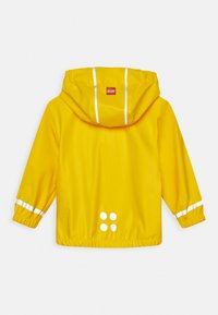 Gul vattentät jacka med huva, elastiska ärmslut, vita reflektionsränder på ärmarna och fyra vita cirkulära detaljer på baksidan.