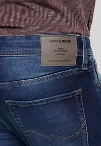 Mörkblå denimjeans med en mjuk textur, med en läderlapp märkt "Jack & Jones" på baksidan och två bakfickor med sömnad.