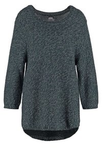 Mörkgrön stickad tröja med vid halsringning, långa ärmar och en något längre baksöm. Texturerad tyg med ett subtilt mönster.