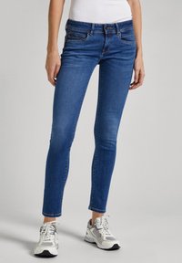 Blå denim skinny jeans med midja i normalhöjd, framfickor och lätt urtvättning. Bärs med grå och vita träningsskor.