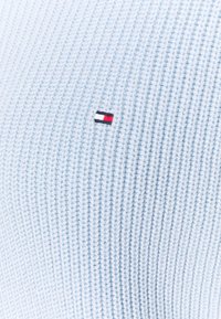 Tessuto a maglia a coste di colore blu chiaro con un piccolo logo cucito con strisce rosse, bianche e blu sul lato sinistro.