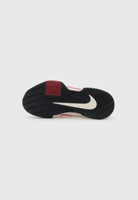 Nike-fottøy med en teksturert svart gummiyttersåle, røde og kremfargede detaljer, med en fremtredende hvit swoosh på en sik-sak-mønstret base.