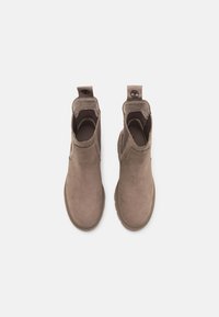 Bottines en suede marron avec un bout arrondi, des panneaux latéraux élastiques et une languette à l'arrière, dotées d'une semelle en caoutchouc texturé.