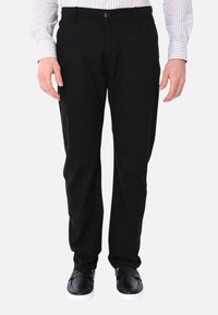 Pantaloni neri in misto cotone con design dritto, dotati di chiusura frontale con bottone e tasche. Indossati con sneakers nere.