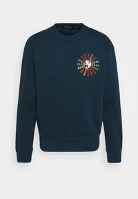 Felpa girocollo di un blu scuro con un colorato ricamo di una testa di orso ruggente e il testo "Scotch & Soda" che la circonda sul lato sinistro del petto.