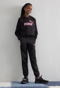 Melnā kapuce ar rozā "PUMA" logo, apvienota ar melnām sporta biksēm, kurām ir zelta "Puma" akcents. Melni sporta apavi noslēdz apģērbu.