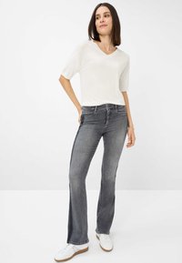 Top corto beige chiaro a maniche corte, jeans grigi a zampa d'elefante e sneakers bianche. Il top ha un collo a V e una consistenza liscia; i jeans mostrano una leggera scoloritura.