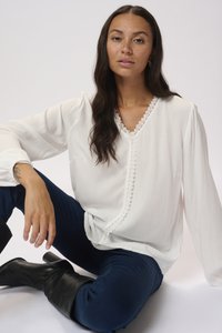 White blouse with lace trim along the neckline and button closure, paired with dark blue jeans and black knee-high boots.