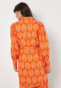 Oranges Kleid mit einem blätterartigen weißen Druck, ausgestattet mit puffärmel und einem taillierten Bund. Hergestellt aus leichtem Stoff, hat es eine lockere Passform.