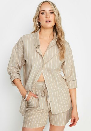 Camisa beig rayada con mangas enrolladas y cierre de botones, combinada con unos pantalones cortos a juego. Tela ligera, corte relajado, diseño casual.