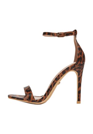 Wysoka sandałka na szpilce o wzorze w panterkę, z paskiem wokół kostki i odkrytymi palcami na białym tle.