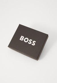 Caixa rectangular preta com textura suave, apresentando a palavra "BOSS" em letras brancas em negrito na frente.