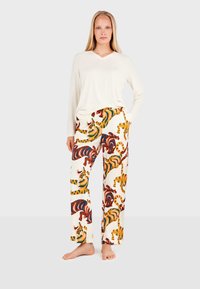Lange mouwen crèmekleurige top in combinatie met wijde broek met een levendig tijgerprint in oranje, bruin en blauw op een witte achtergrond.