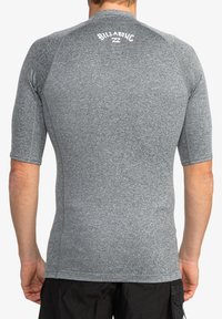 Rash guard gris de manga corta con un diseño ajustado, textura suave y detalle del logo en blanco en la parte posterior cerca del cuello.