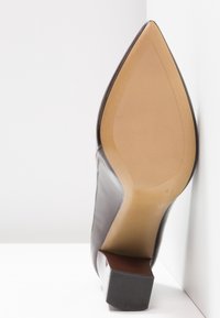 Chaussure habillée en cuir marron à bout pointu, montrant une semelle beige texturée et un talon carré épais sur fond blanc.