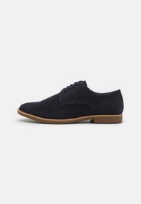 Chaussures bleu marine à lacets en tissu texturé avec un bout lisse et une semelle en caoutchouc, présentant un détail de surpiqûre contrastante subtile.