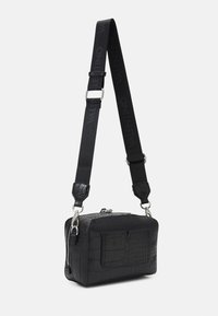 Černá crossbody taška s texturovaným krokodýlím vzorem, stříbrným zipem a nastavitelným popruhem s logem "VALENTINO". Obdélníkový tvar.