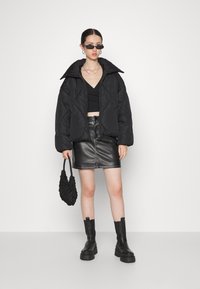 Plumífero negro con gran cuello, cierre de botón, combinado con un top negro corto, falda mini de cuero y botas gruesas negras. Incluye bolso negro.