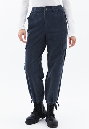 Marineblauwe cargobroek van zachte stof met een elastische taille, opgerolde enkels en zijzakken. Gecombineerd met zwarte legerlaarzen.