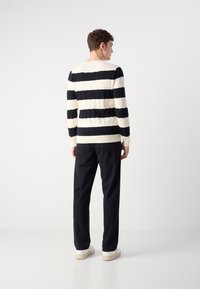 Megzta megztinis su jūrų mėlynos ir kreminės spalvos horizontaliomis juostomis; turi kabliuko raštą, apvalų kaklą ir raštuotas rankoves. Pora su juodomis kelnėmis ir sportbačiais.