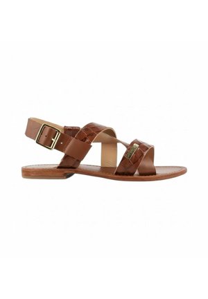 Sandale plate en cuir marron avec des brides croisées, une boucle dorée sur la bride de cheville, et une petite étiquette de marque dorée sur la bride avant.