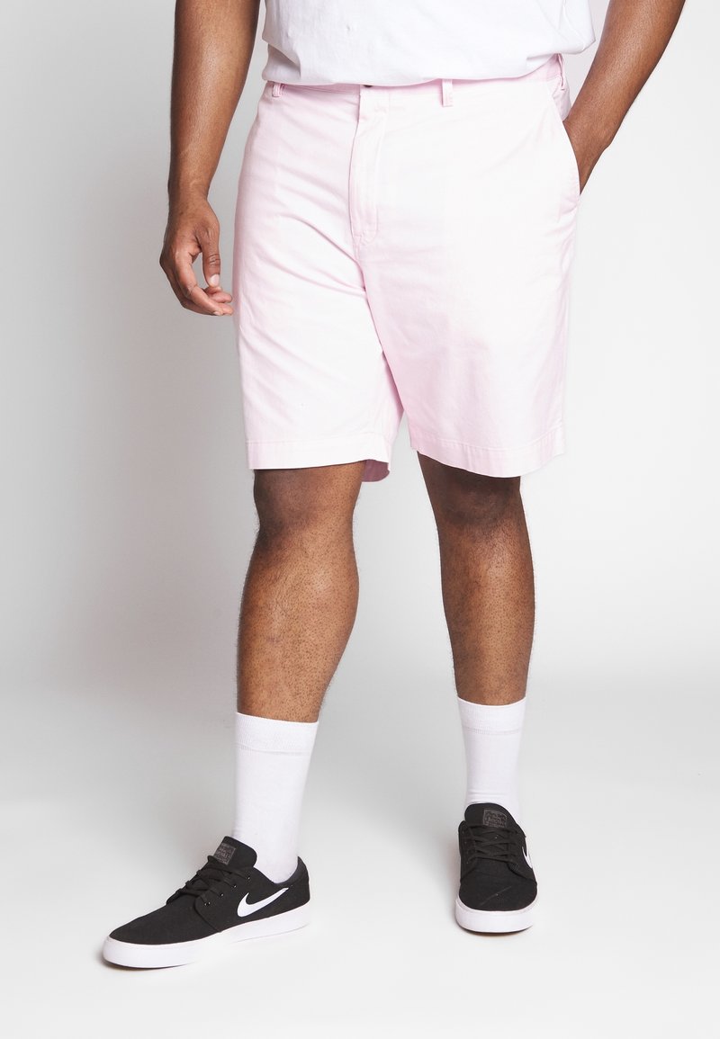 Svetle růžové bavlněné kraťasy s volným střihem, s bočními kapsami. Nosené s černými teniskami a bílými kotníkovými ponožkami.