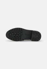 Semelle de chaussure noire avec des motifs profonds hexagonaux et rectangulaires, conçue pour l'adhérence et la traction, présentée sur un fond blanc uni.