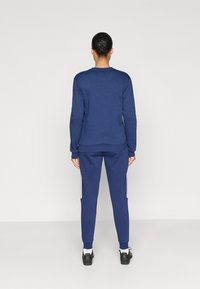 Φούτερ και παντελόνι φόρμας σε ναυτικό μπλε χρώμα από απαλό ύφασμα φλίς. Το παντελόνι φόρμας έχει λευκές πλευρικές ρίγες και ριμπ μανσέτες για άνετη εφαρμογή.