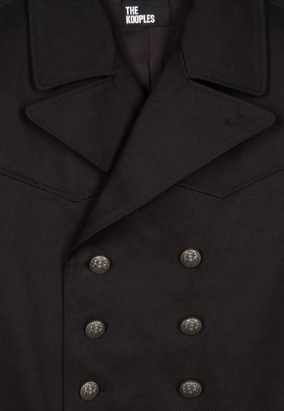 Schwarzer doppelt knöpfiger Mantel mit breitem Kragen, silbernen dekorativen Knöpfen und glattem Textil. Markenlabel am Ausschnitt sichtbar.