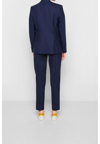 Marinblå kostym med en skräddarsydd kavaj och raka byxor, kombinerad med ljusa skor med gula accenter. Slät, klassisk design.