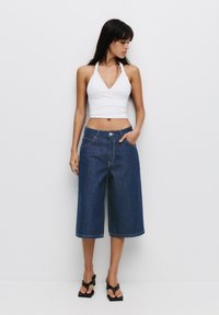Biała halter neck crop top zestawiona z szerokimi, ciemnoniebieskimi dżinsowymi kulotami, z przednimi kieszeniami i zapięciem na guzik. Czarne sandały na obcasie.