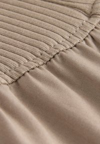 Lys beige stof med et struktureret ribbet mønster øverst og glatte folder nedenfor, med fine sømme langs kanten.