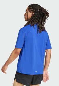 Blå sporttröja med kort ärm i fukttransporterande material, med rundad halsringning och avslappnad passform, ihop med svarta shorts.