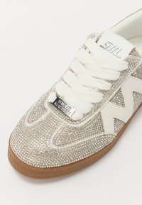 Glitrende sølv sneakers med hvite detaljer, prydet med rhinestones, teksturert overflate, hvite snører og brun gummisåle.