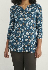 Tunic blu con motivo fogliare in teal, bianco e marrone. Presenta un collo a V e maniche a tre quarti. Tessuto morbido con un fit rilassato.
