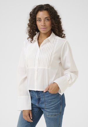 Witte katoenen shirt met geplooide voorkant, knoopsluiting en lange belmouwen, gecombineerd met blauwe jeans.