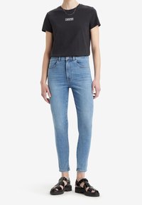 Camiseta negra con un logo blanco de Levi's, jeans ajustados de mezclilla azul claro y sandalias negras de tiras. Tela de algodón suave y mezclilla resistente.