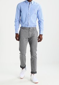 Camisa abotonada a rayas de color azul claro, pantalones grises tapered y zapatillas blancas con acentos rojos. Características incluyen cuello abotonado y puños enrollados.