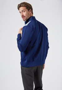 Navy blue zip-up jacket with a textured surface, contrasting light blue accents on shoulders, and ribbed cuffs. Features side pockets.