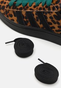 Leopardmönstrade sneakers i tan och svart mocka med tealfärgade snören. Två rullade svarta snören placerade under. Svart gummisula.