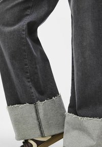 Mörkgrå denimbyxor med breda uppvikningar som har ett grått tygöverdrag och rå kant. Tydlig sömnadsdetalj längs kanten på uppvikningarna.