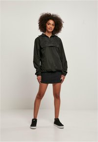 Zwarte, lichte pulloverjas met een halve rits, voorzak en elastische manchetten, gecombineerd met een denimrok en zwarte sneakers.