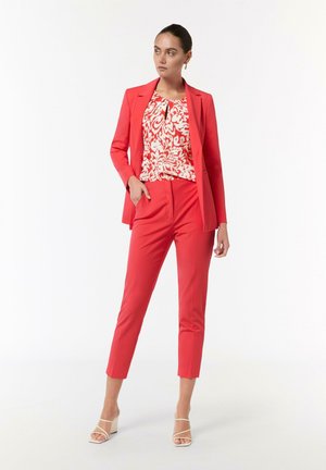 Red tailored suit with a fitted blazer and cropped pants. The blouse features a white and red floral pattern. Shoes are nude strappy sandals.