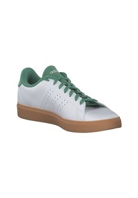Zapatilla deportiva blanca con detalles en verde, parte superior de cuero texturizado, detalles laterales perforados y suela de goma marrón.