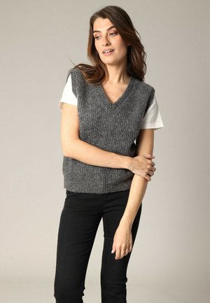 Un gilet sans manches en tricot gris avec un col en V, associé à un t-shirt blanc. Le gilet présente un design ribbed texturé et une silhouette ajustée.