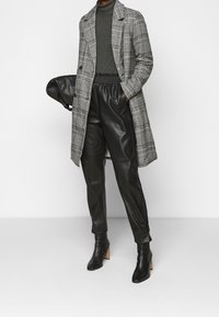 Długi szary i czarny płaszcz w kratę, noszony na ciemnym golfie, w zestawieniu z czarnymi spodniami z sztucznej skóry i botkami na wysokim obcasie z wąskim noskiem.