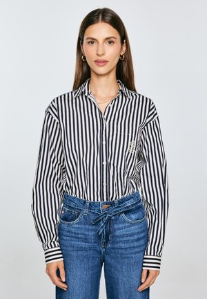 Striped button-up shirt in navy and cream with a chest pocket, paired with high-waisted blue denim jeans featuring a drawstring and relaxed fit.